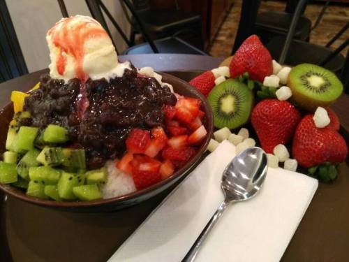 A bowl of shaved ice topped with red bean, ice cream, and fresh fruit, alongside a plate of mixed strawberries and kiwi.