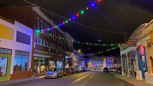 A colorful street at night, lined with buildings and festive lights strung overhead, creating a vibrant atmosphere.