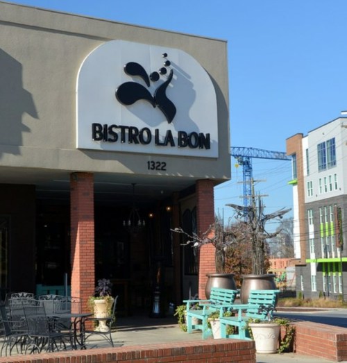 Exterior of Bistro La Bon, featuring a sign, outdoor seating, and modern buildings in the background.