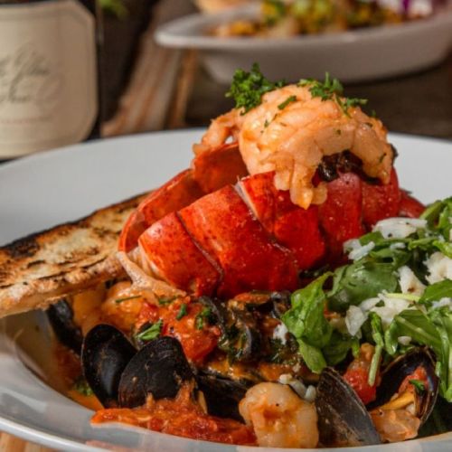 A vibrant seafood dish featuring lobster, shrimp, mussels, and fresh herbs, served with toasted bread.