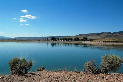A serene lake surrounded by shrubs and mountains under a clear blue sky.