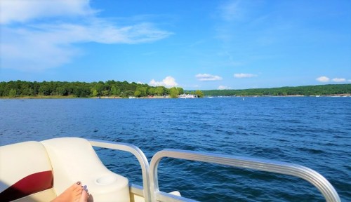 A scenic view of a lake with trees in the background, seen from a boat, under a clear blue sky.