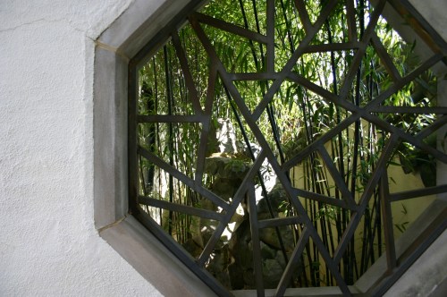 An octagonal window with a geometric metal frame, revealing a lush bamboo garden outside.