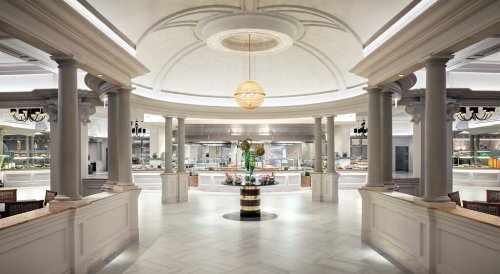 Elegant restaurant interior featuring a central floral arrangement, marble flooring, and decorative columns under a chandelier.