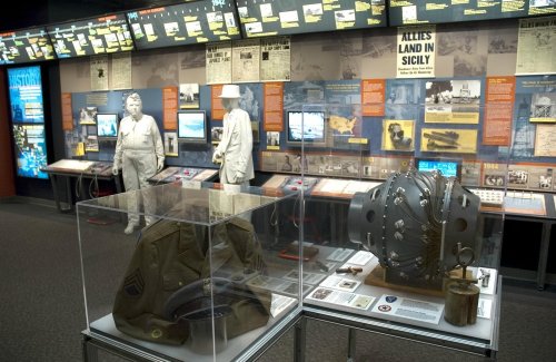 Exhibit showcasing WWII artifacts, including uniforms and equipment, with informative displays in the background.