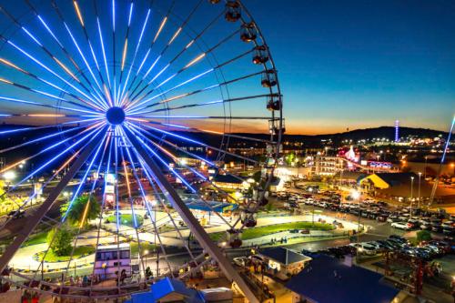 A vibrant ferris wheel illuminated at night, overlooking a bustling amusement park and parking lot.