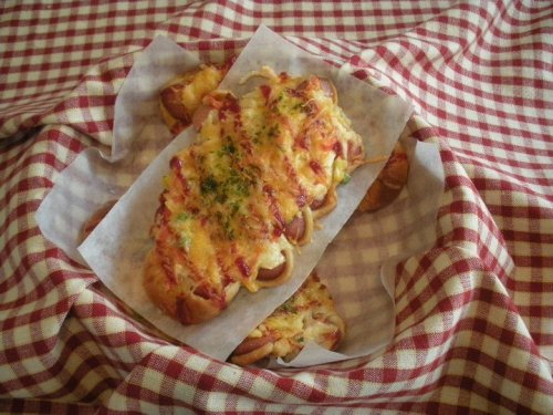 A freshly baked cheesy bread topped with herbs, served in a basket lined with parchment paper on a checkered tablecloth.