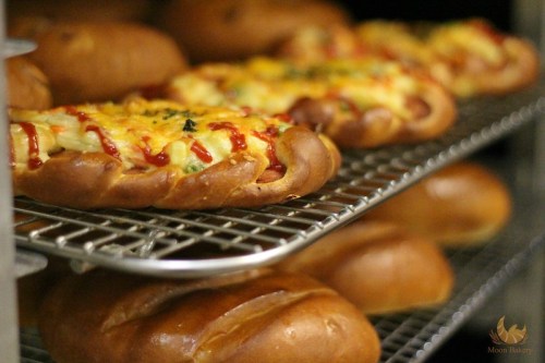 Freshly baked bread rolls topped with cheese, vegetables, and ketchup, displayed on a cooling rack.