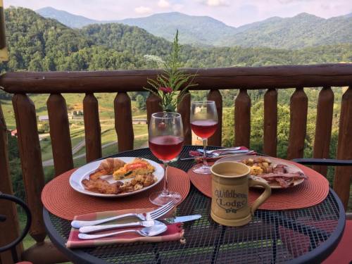 A scenic view of mountains from a balcony table set with plates of food and drinks, surrounded by greenery.