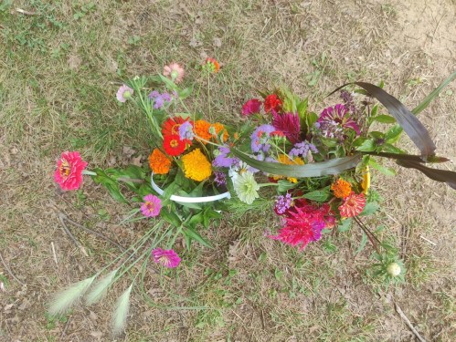 A vibrant arrangement of colorful flowers on grassy ground, featuring various blooms in shades of pink, orange, and purple.