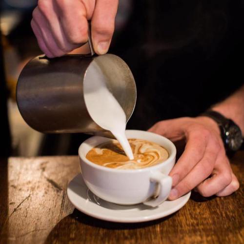 A barista pours steamed milk into a cup of coffee, creating a beautiful latte art design.
