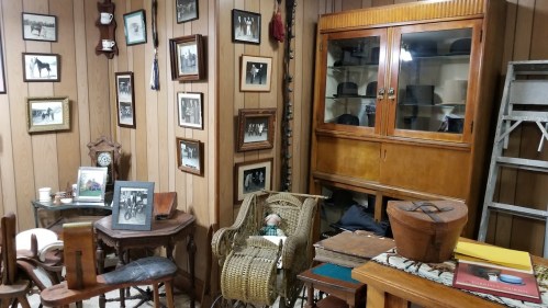 A vintage room filled with wooden furniture, framed photos, and a glass cabinet displaying various items.