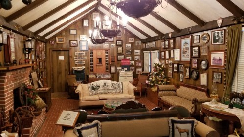 Cozy room with wooden walls, vintage decor, framed photos, and a Christmas tree, featuring comfortable seating.