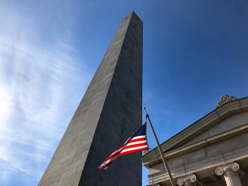 A tall stone obelisk against a blue sky, with an American flag waving in the foreground.