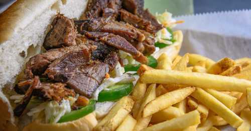 A close-up of a sandwich filled with sliced beef, peppers, and lettuce, served with a side of golden French fries.