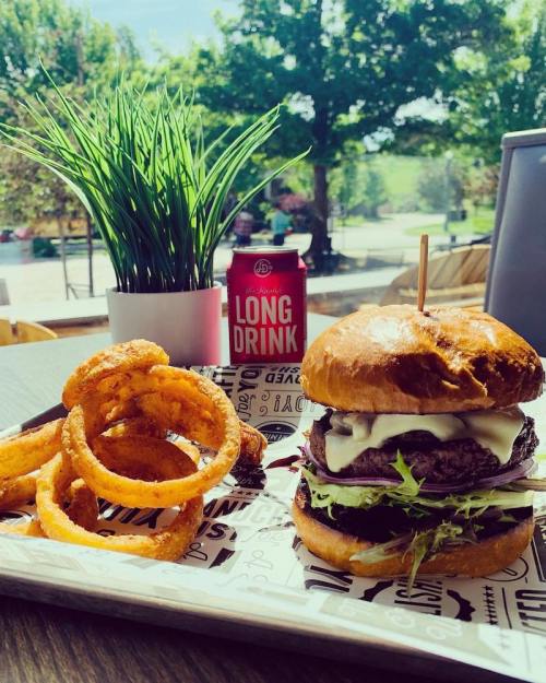 A delicious burger with lettuce and cheese, served with onion rings and a can of long drink, set in a sunny outdoor scene.