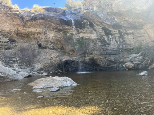 A serene rocky landscape featuring a small waterfall cascading into a clear pool surrounded by stones and vegetation.