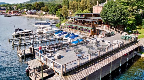 Aerial view of a waterfront restaurant with outdoor seating, boats docked, and lush greenery in the background.