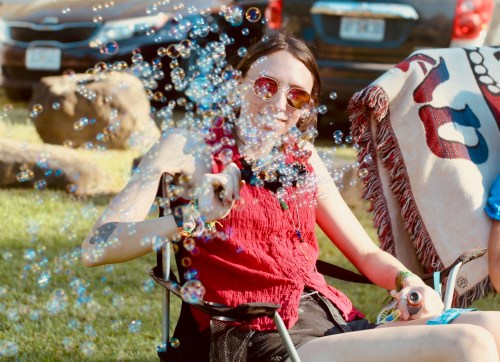 A person in sunglasses sits in a chair, surrounded by bubbles, enjoying a sunny day outdoors.
