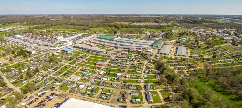 Aerial view of a large outdoor event with numerous tents, vehicles, and green spaces in a rural setting.