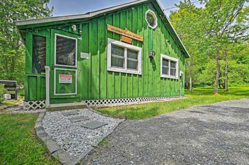 A bright green cabin with a wooden sign, surrounded by trees and a gravel path leading to the entrance.