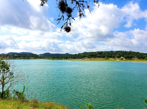 A serene lake surrounded by lush greenery and hills under a partly cloudy sky.