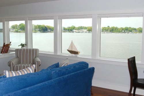 Cozy living room with blue couch and striped chair, featuring large windows overlooking a calm waterfront view.