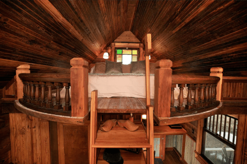 Cozy loft bedroom with wooden walls, a circular railing, and a ladder leading down to a lower level.