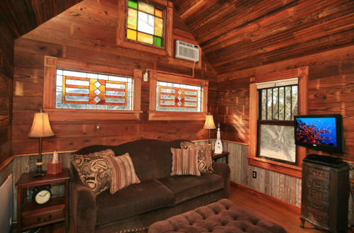 Cozy wooden interior of a cabin with stained glass windows, a sofa, and a TV, creating a warm, inviting atmosphere.
