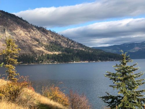 Scenic view of a calm lake surrounded by mountains and trees under a partly cloudy sky.