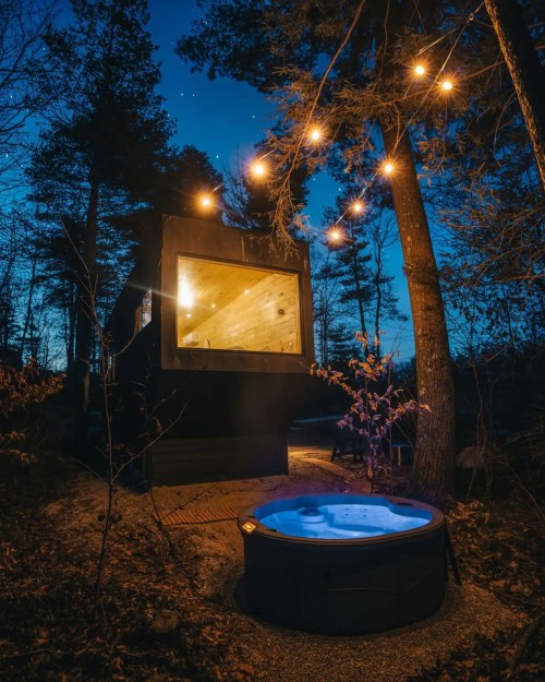 A cozy cabin at night with a hot tub outside, surrounded by trees and string lights illuminating the scene.