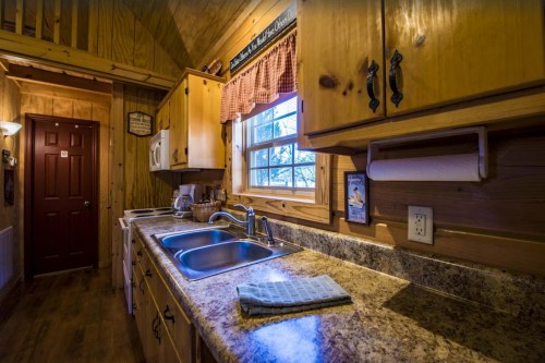 Cozy wooden kitchen with granite countertops, a double sink, and warm lighting, featuring rustic decor and appliances.