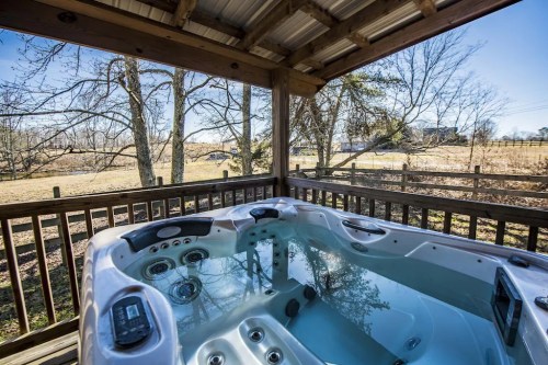 A hot tub on a wooden deck overlooking a serene landscape with trees and a fence in the background.