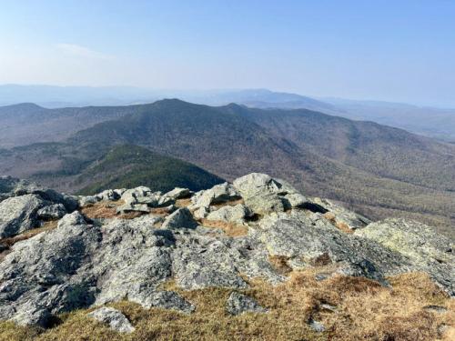 A panoramic view of rolling mountains and rocky terrain under a clear blue sky.