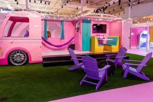A colorful pink and teal camper van interior with lounge chairs on green grass, set in a bright, modern space.