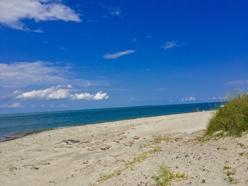 A serene beach scene with soft sand, gentle waves, and a clear blue sky dotted with clouds.