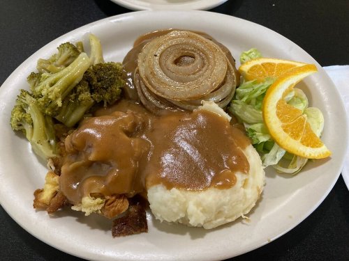 A plate of food featuring mashed potatoes with gravy, sautéed onions, broccoli, salad, and orange slices.