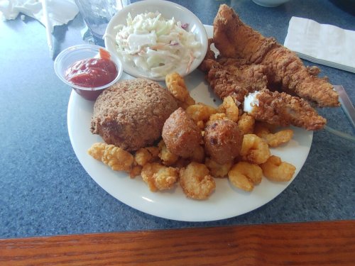 A plate of fried fish, coleslaw, hushpuppies, and tater tots with a side of ketchup.