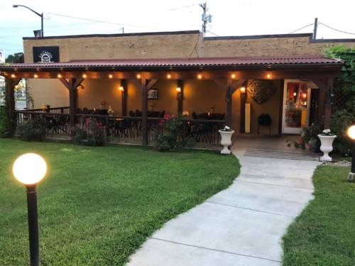 A cozy outdoor dining area with string lights, surrounded by greenery and a pathway leading to the entrance.