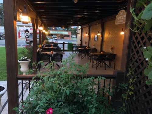 A cozy outdoor dining area with tables and chairs, surrounded by greenery and softly lit by hanging lights.