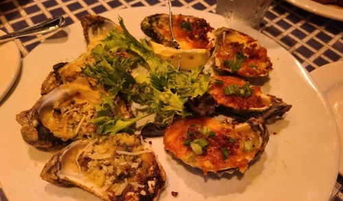 A plate of baked oysters topped with cheese, herbs, and garnished with lemon and greens.