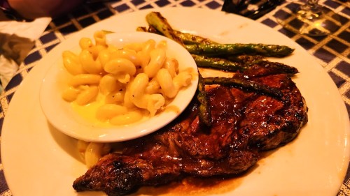 A plate featuring a grilled steak, macaroni and cheese, and asparagus on a checkered tablecloth.