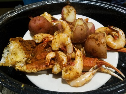 A plate of seasoned shrimp and red potatoes, served in a black dish.