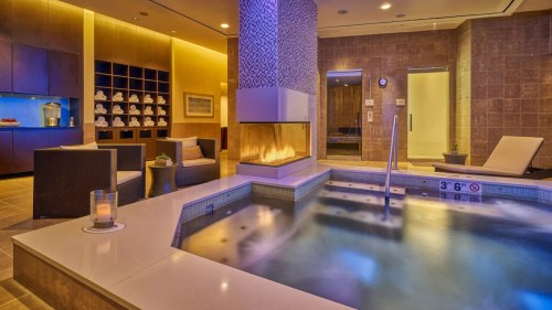 A serene spa area featuring a hot tub, modern seating, and a cozy fireplace with soft lighting.
