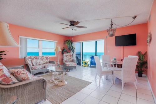 Bright coastal living room with floral furniture, ocean views, and a dining area, featuring light colors and tropical decor.