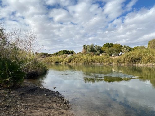 A calm river surrounded by lush greenery and trees under a partly cloudy sky.