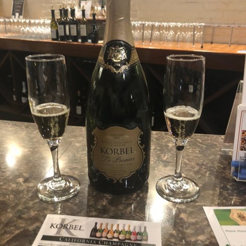 A bottle of Korbel champagne with two filled flutes on a bar counter, alongside a menu card.
