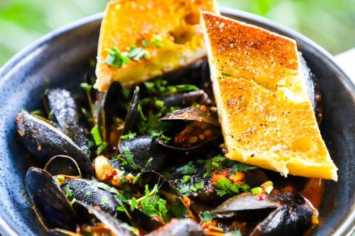 A bowl of mussels in a spicy sauce, topped with fresh herbs and served with two pieces of toasted bread.