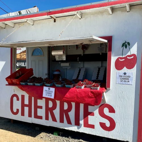 A roadside stand with a sign reading "Cherries" and baskets of fresh cherries for sale.