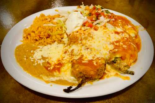 A plate of enchiladas topped with cheese and sauce, served with rice, salad, and sour cream.